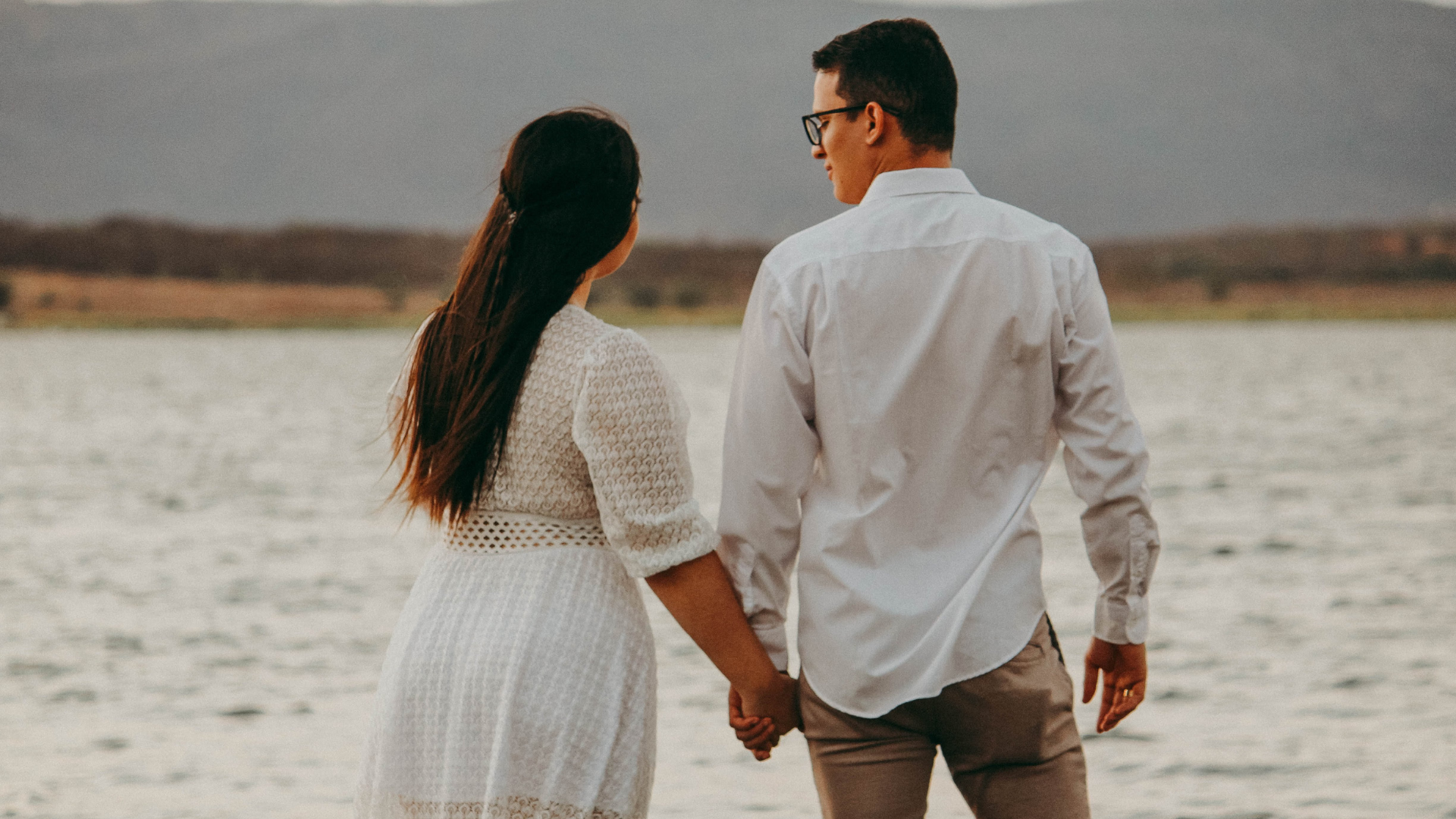 A couple holding hands while looking at the peaceful landscape by the water.
